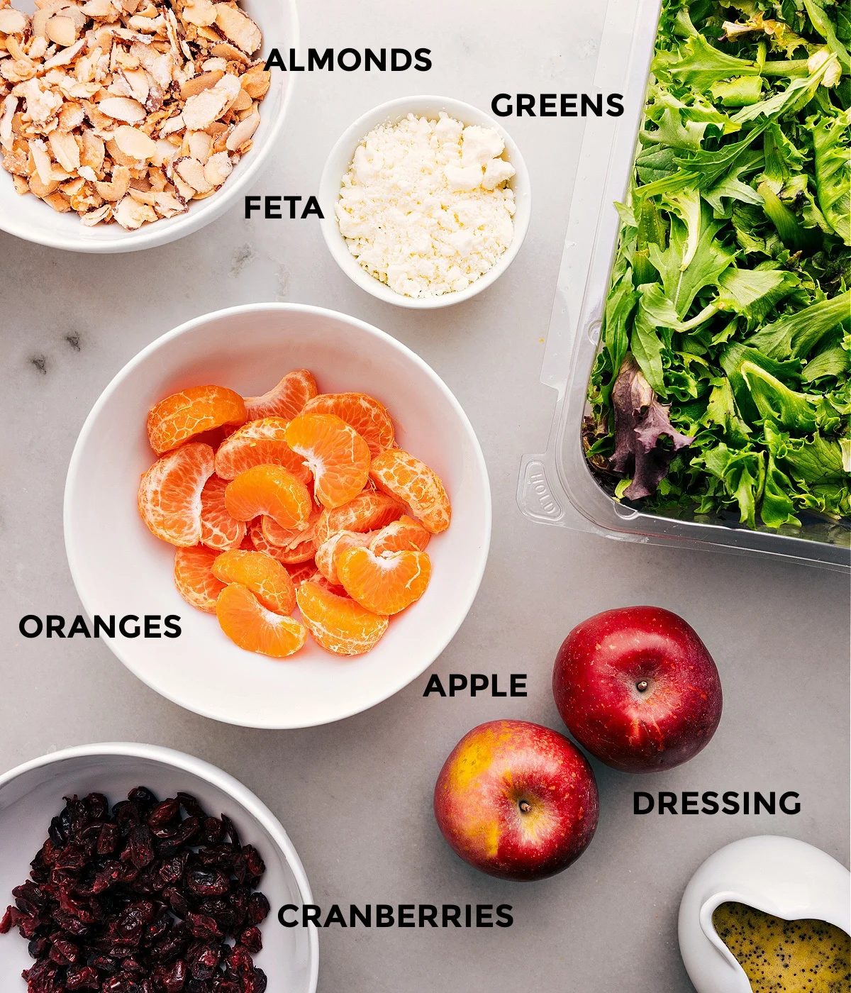 Prep all the ingredients for this recipe, including almonds, greens, fruit, feta, dressing, and dried cranberries, for straightforward assembly.