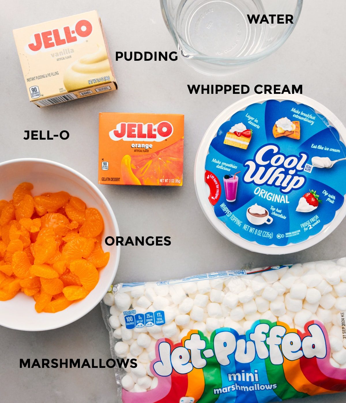 All the ingredients for this recipe including mandarins, jell-o, cool whip, and mini marshmallows prepped out for straightforward assembly.