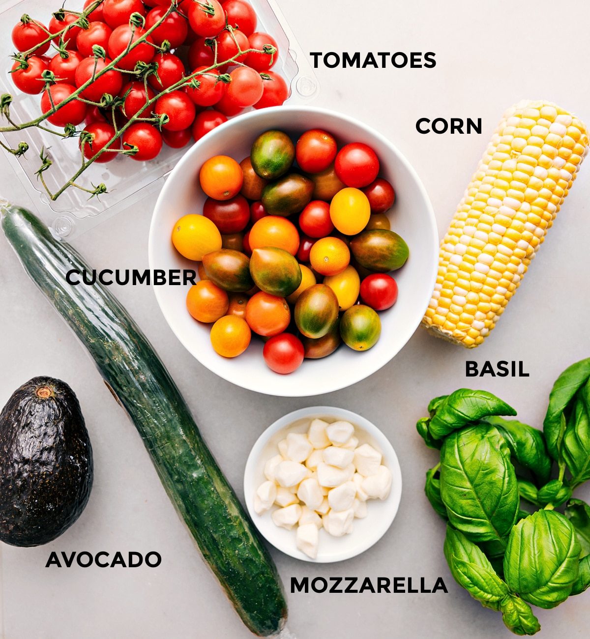 All the ingredients for this recipe are prepped for straightforward assembly, including the tomatoes, corn, cucumber, basil, mozzarella, and avocado.
