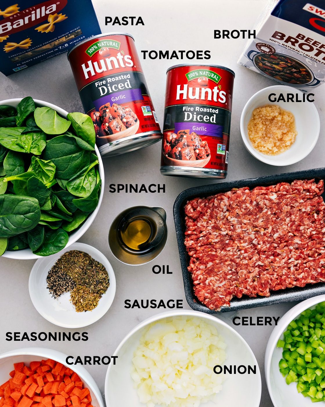 All the ingredients—beef broth, garlic, tomatoes, pasta, sausage, spinach, oil, seasonings, and veggies—are prepped for straightforward assembly.