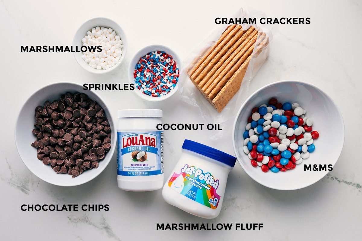 All the ingredients in this recipe prepped out for straightforward assembly including the marshmallows, sprinkles, chocolate chips, coconut oil, marshmallow fluff, M&Ms, and graham crackers.