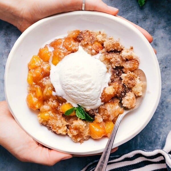 Sweet and satisfying peach cobbler in a bowl with a scoop of vanilla ice cream on top.