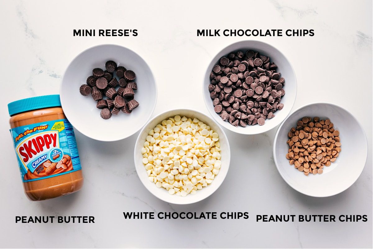 Ingredients prepped in small bowls for straightforward assembly including peanut butter, mini Reese’s cups, white chocolate chips, milk chocolate chips, and peanut butter chips.