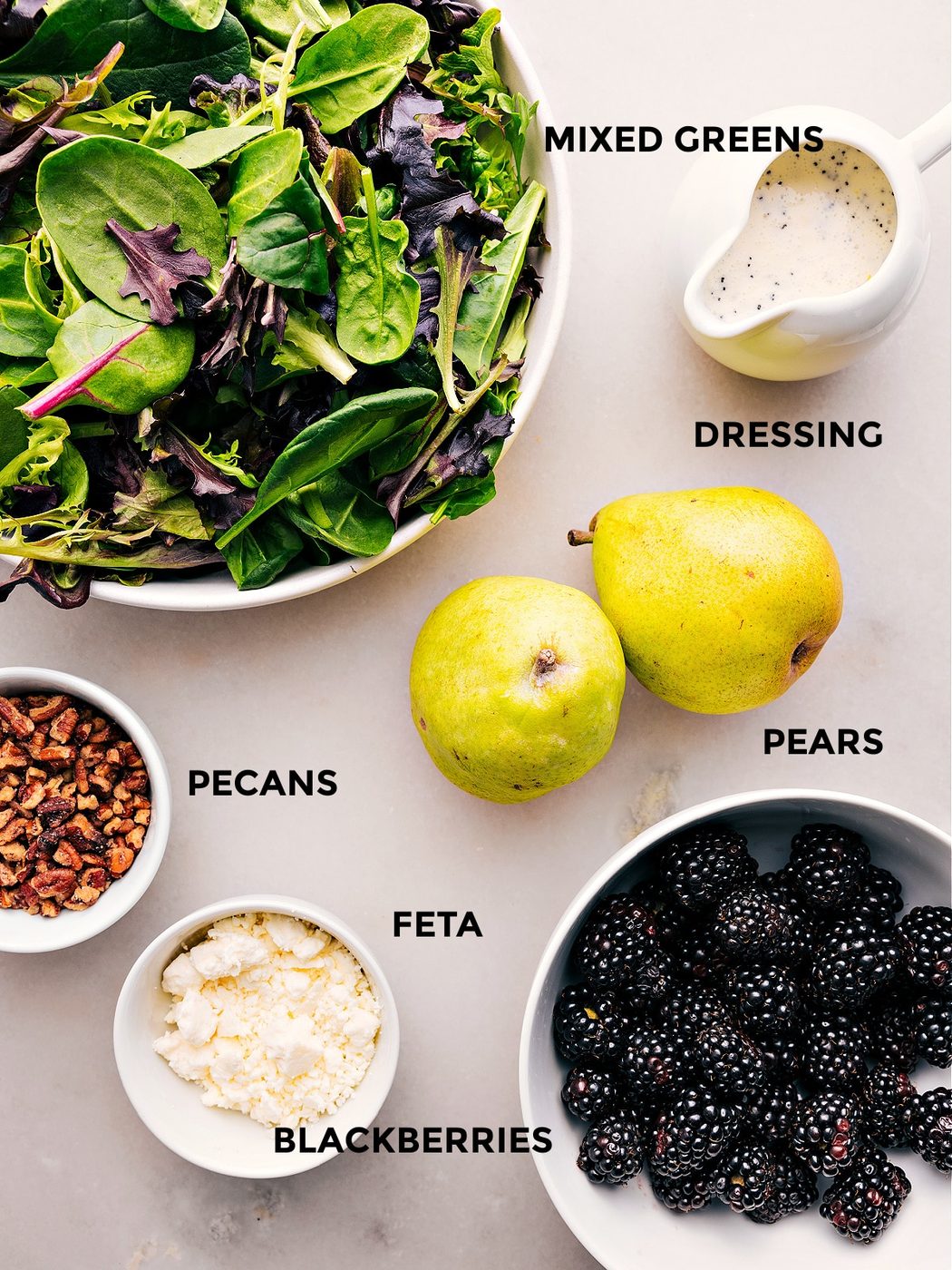 All the ingredients in this recipe are prepped for straightforward assembly, including the dressing, greens, pears, blackberries, feta, and pecans.