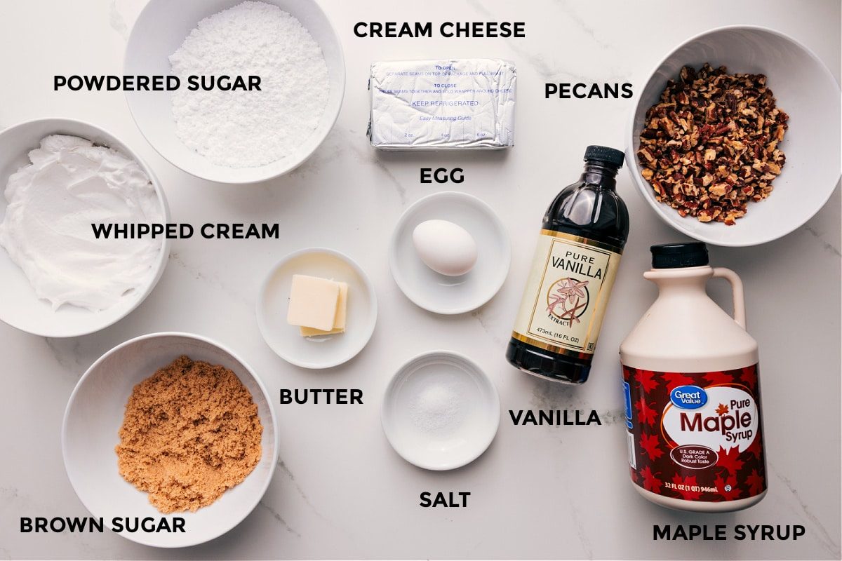All the ingredients in pecan pie dip laid out for straightforward assembly including the whipped cream, brown sugar, butter, powdered sugar, egg, cream cheese, salt, vanilla, pecans, and maple syrup.