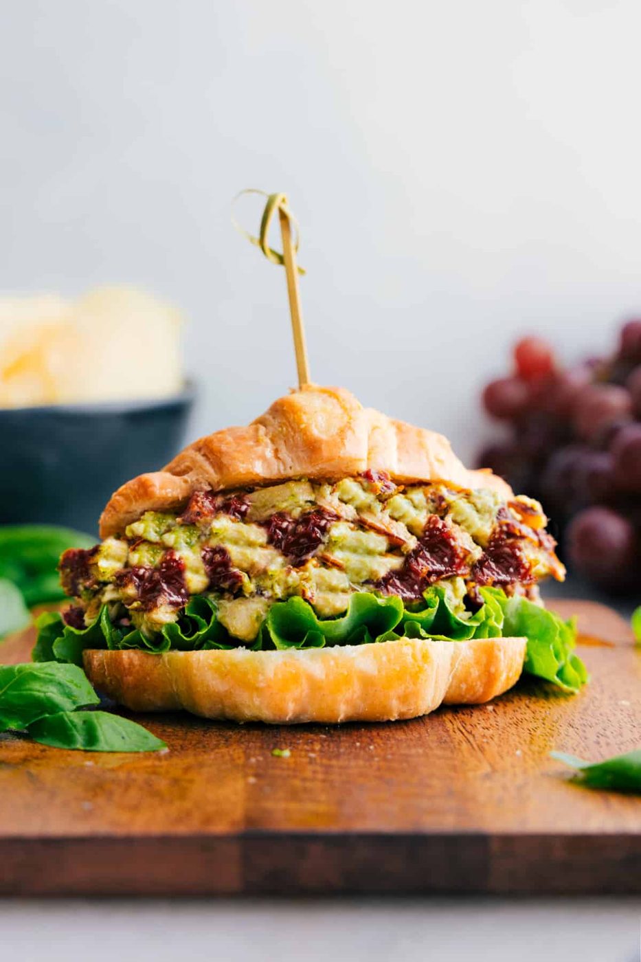 Sandwich with pesto chicken salad in side; grapes and chips in background