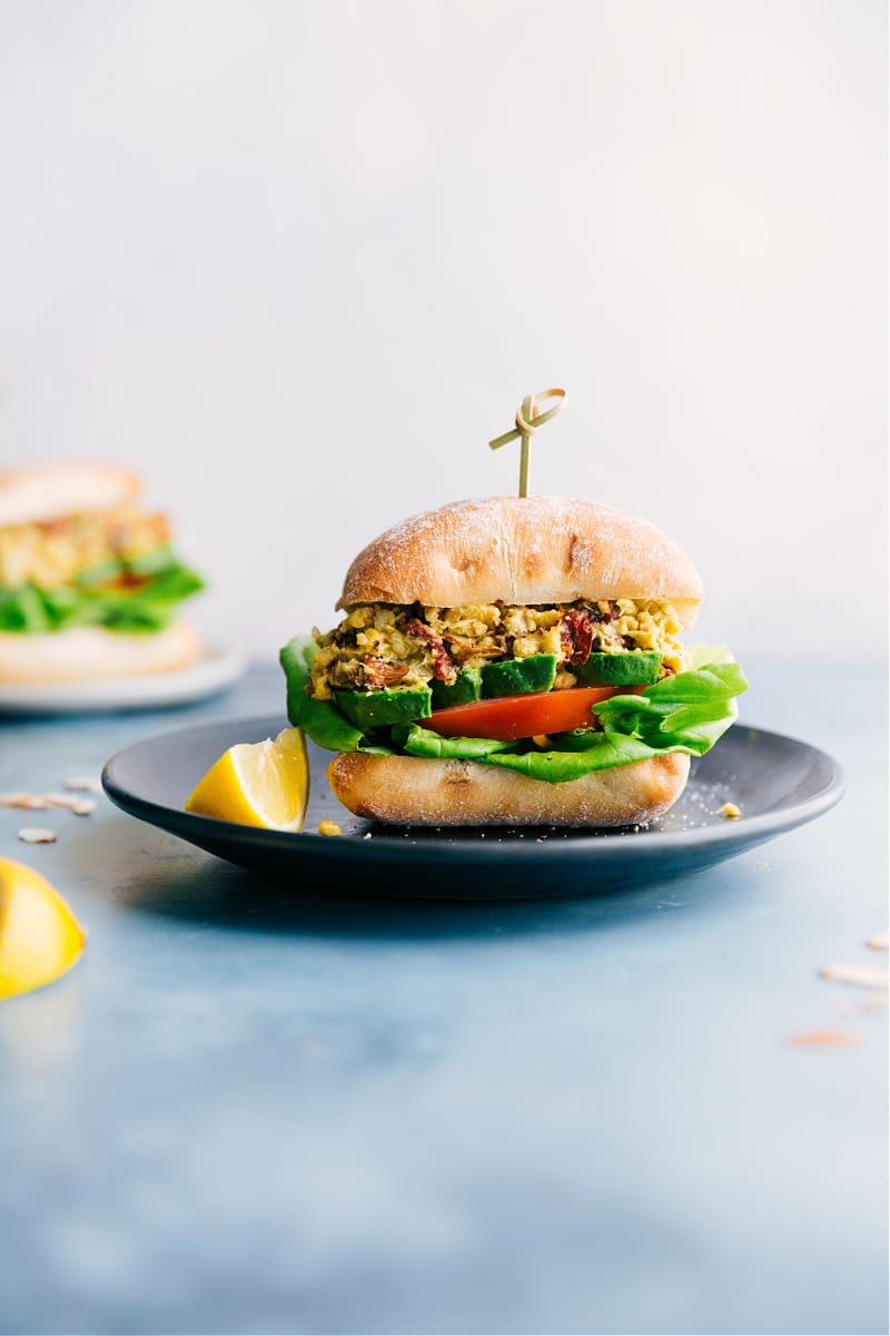 Pesto Chickpea Sandwiches in a ciabatta bun with avocado, tomatoes, and lettuce, served on a plate.