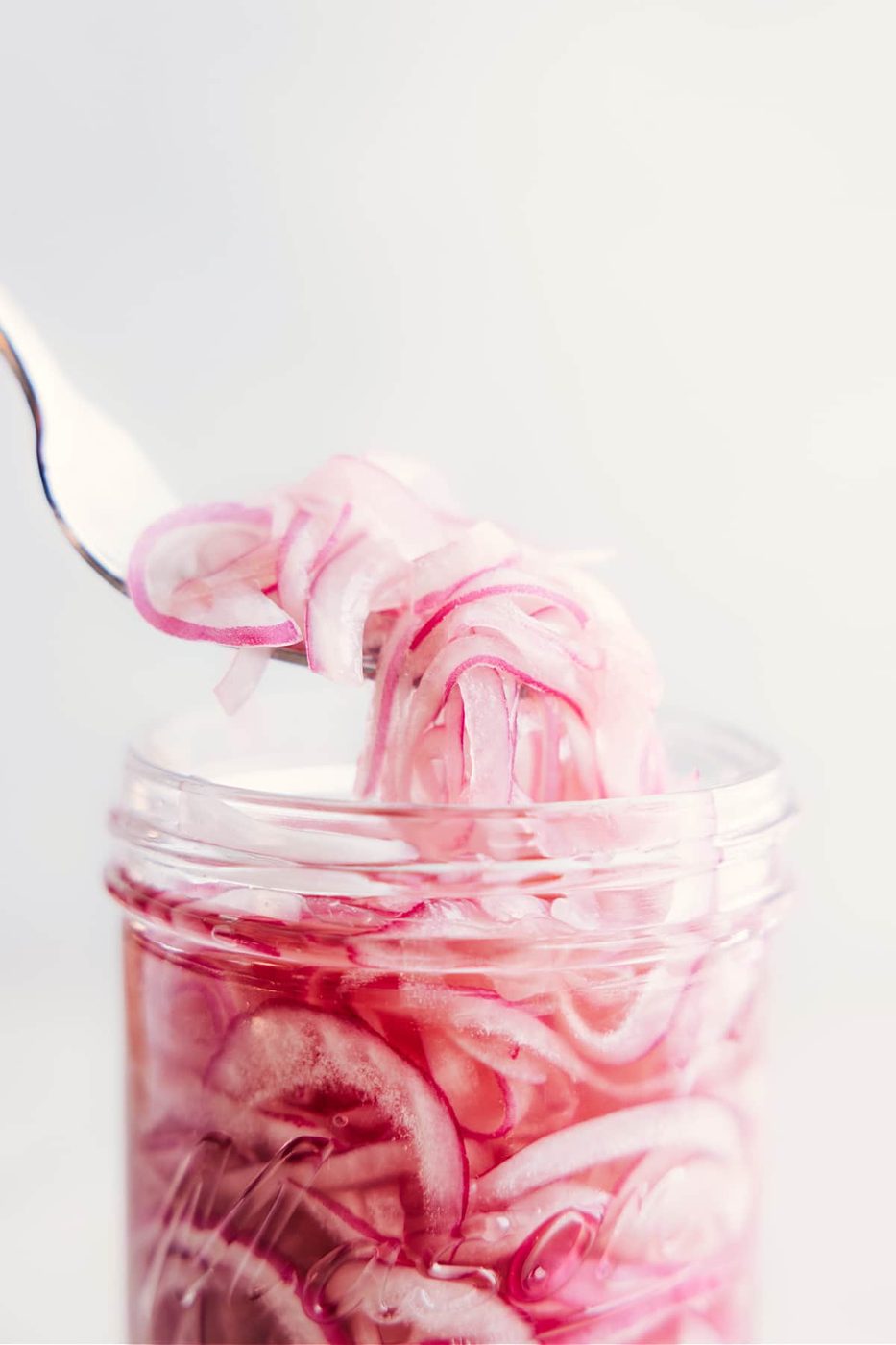 A forkful of pickled red onions being picked up out of the jar.