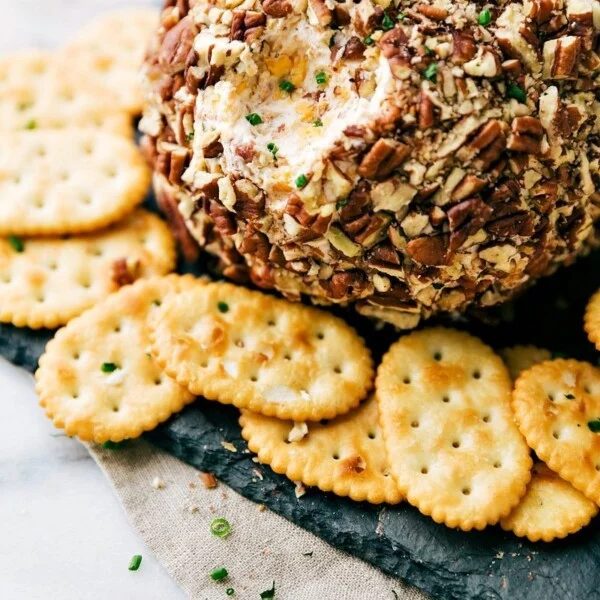 A gorgeous cheese ball with crackers on the side, and a bite scooped out of it, ready to be enjoyed as both a satisfying and visually appealing snack.