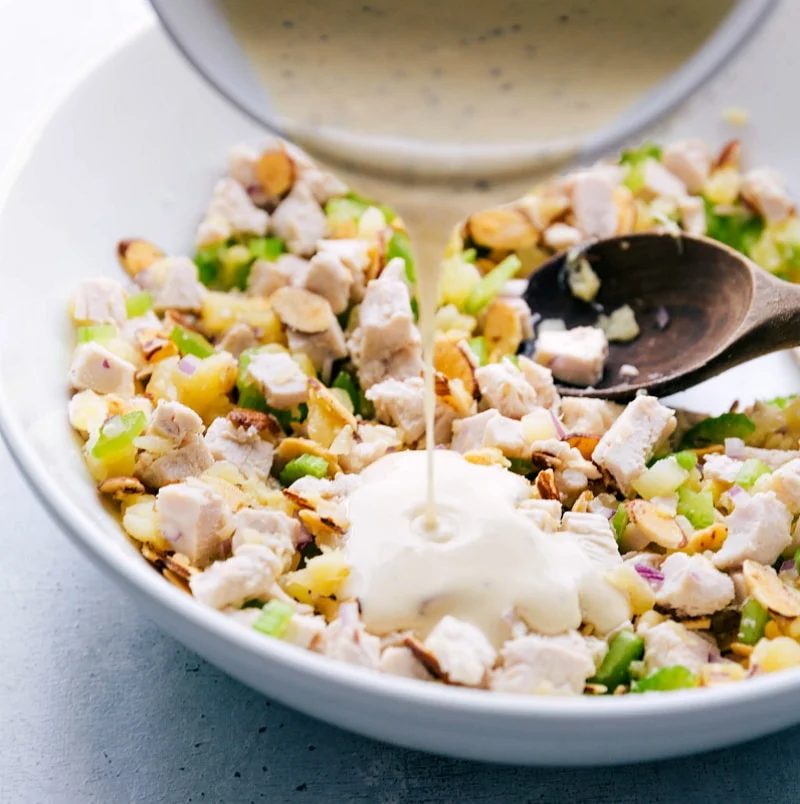 Dressing being poured over the chicken salad with pineapple, ready to be mixed for a satisfying meal.