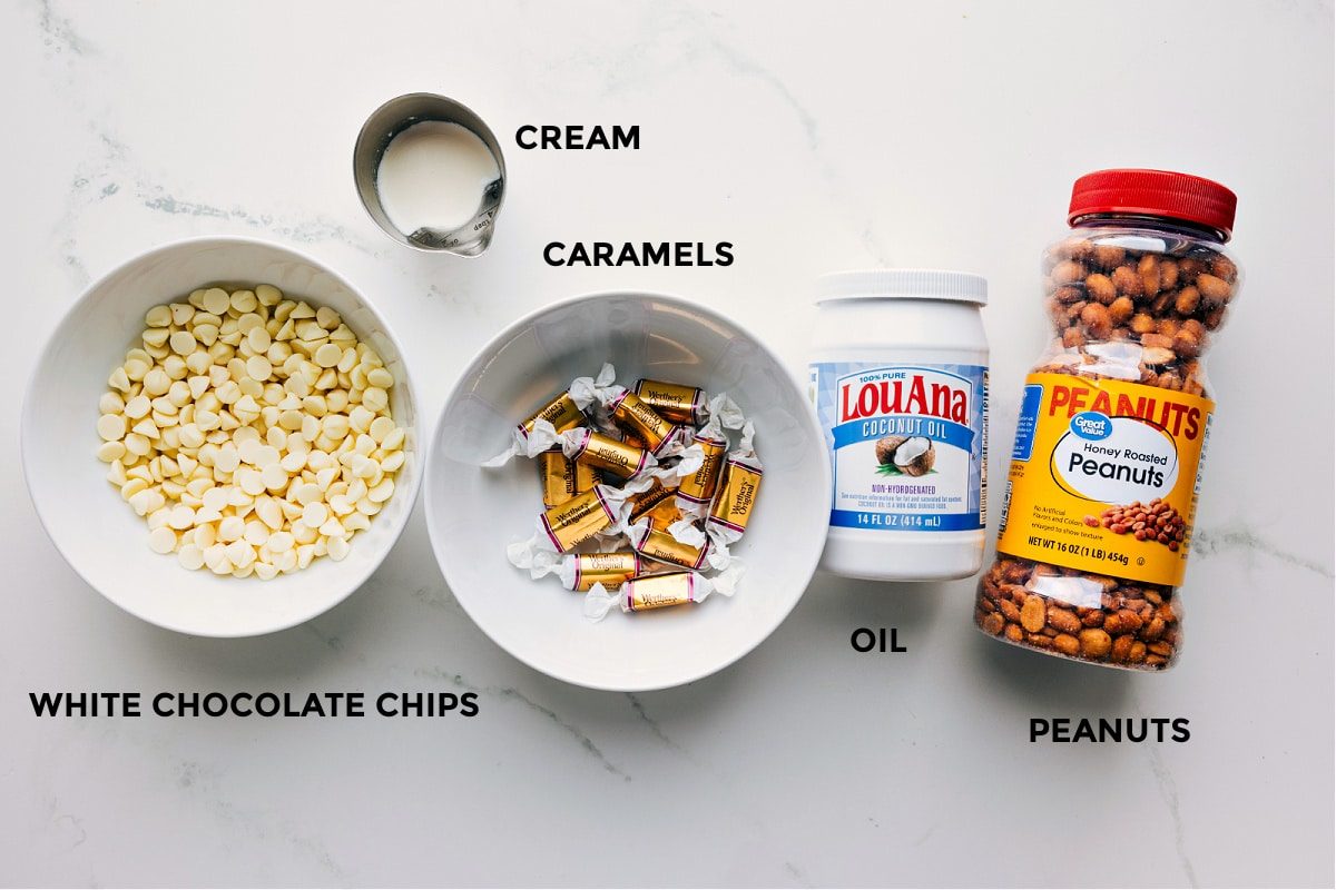 Ingredients in this recipe prepped out for straightforward assembly including the white chocolate chips, cream, caramels, oil, and peanuts.