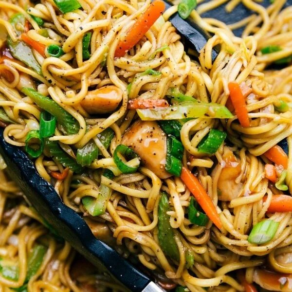Chicken chow mein in a skillet with tongs, filled with fresh vegetables, evenly cooked and seasoned.