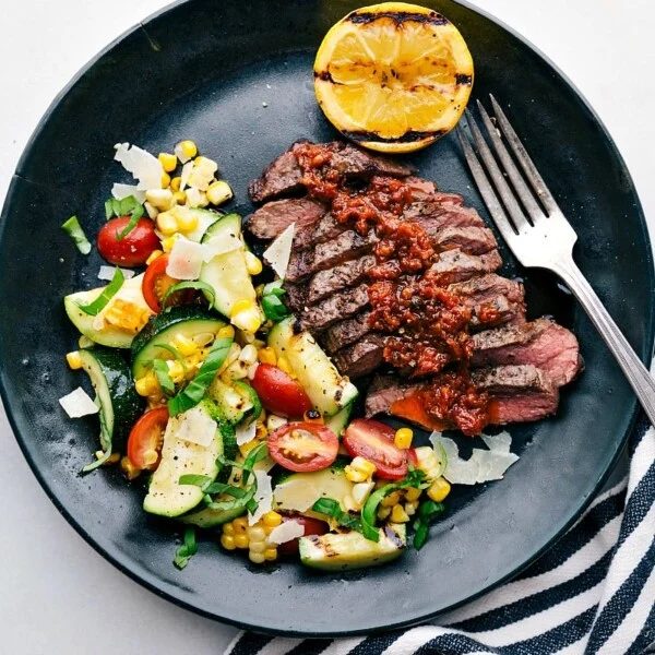 A succulent and tender grilled flat iron steak served with a refreshing zucchini and corn salad on the side, promising a satisfying and satisfying meal.