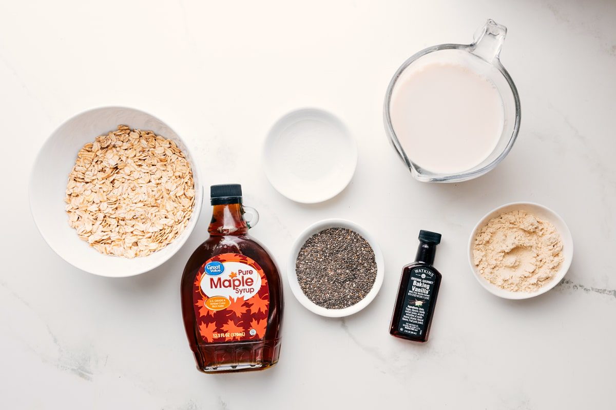 All the ingredients in this recipe prepped out for straightforward assembly including the oats, maple syrup, chia seeds, milk, protein powder, vanilla, and salt.