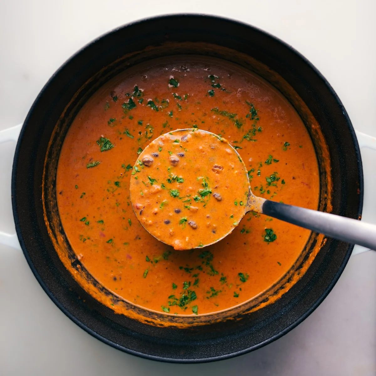 Overhead view of Pumpkin Black Bean Soup in a pot with a ladle scooping a serving.