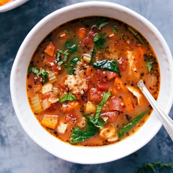 A bowl of hearty slow cooker chicken quinoa soup, with chicken, quinoa, vegetables, and herbs.