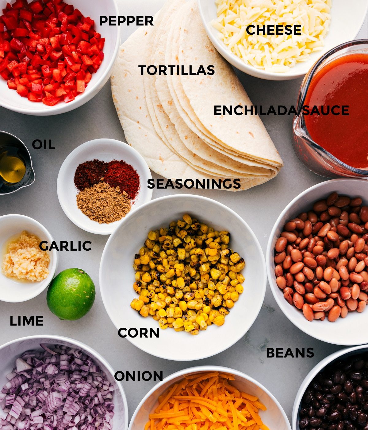 All the ingredients prepped for straightforward assembly, including veggies, tortillas, sauce, corn, cheese, seasonings, and beans.
