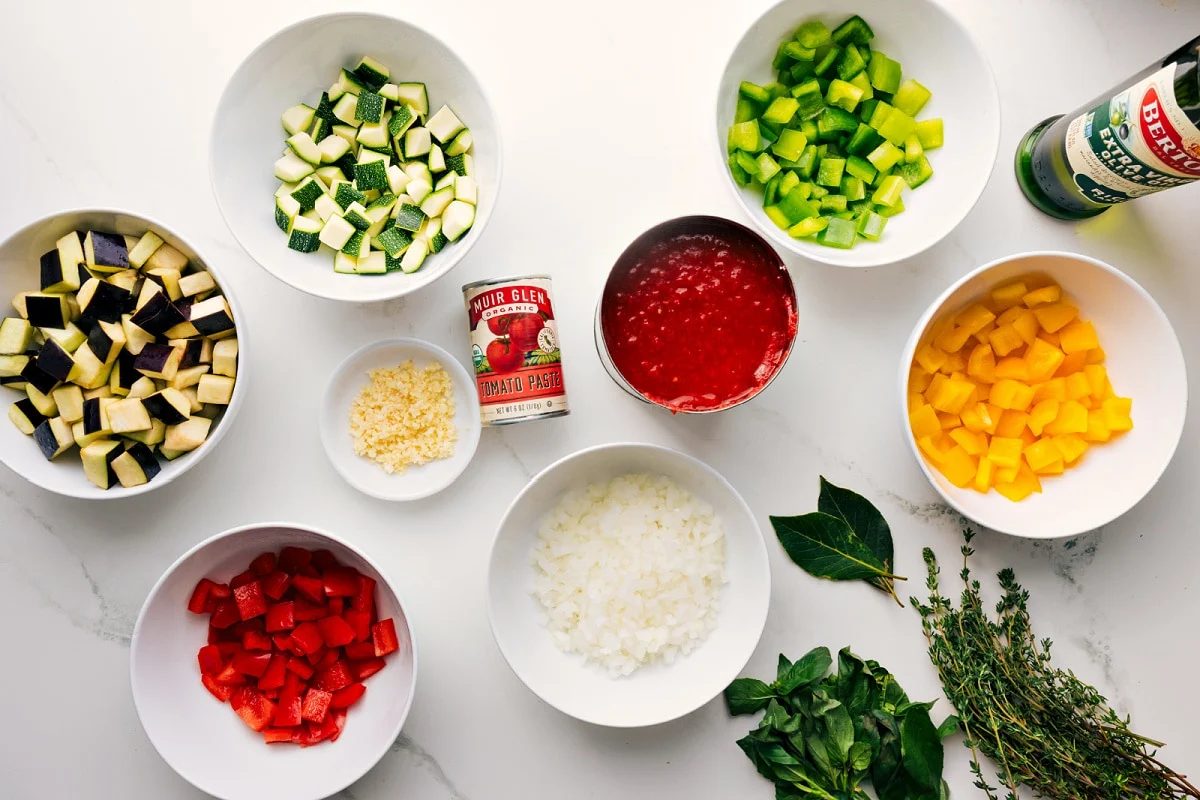 All the ingredients in this recipe prepped out for straightforward assembly including the veggies, tomatoes, oil, garlic, tomato paste, and fresh herbs.