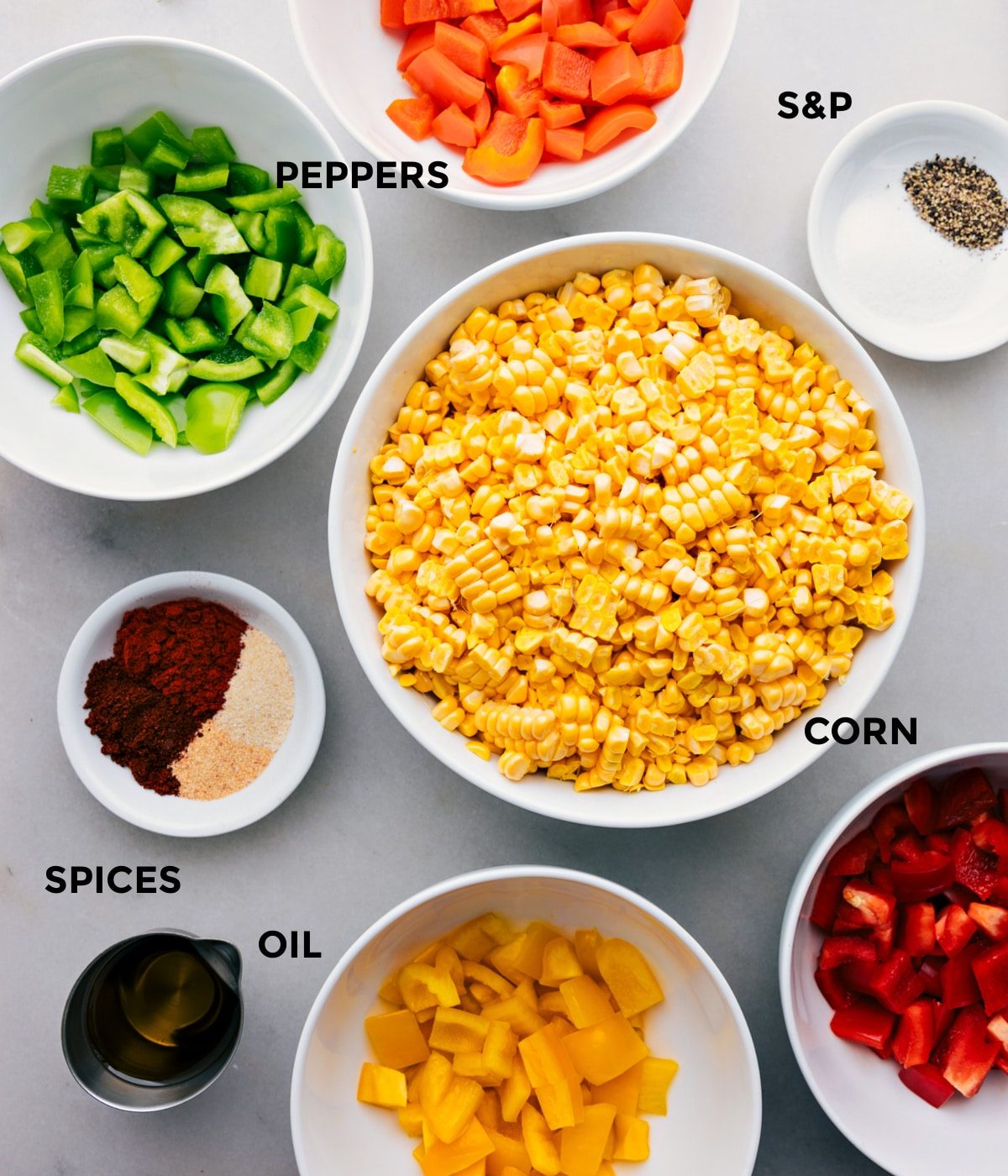 All the ingredients in this recipe including the corn, peppers, oil, spices, and seasonings prepped out for straightforward assembly.