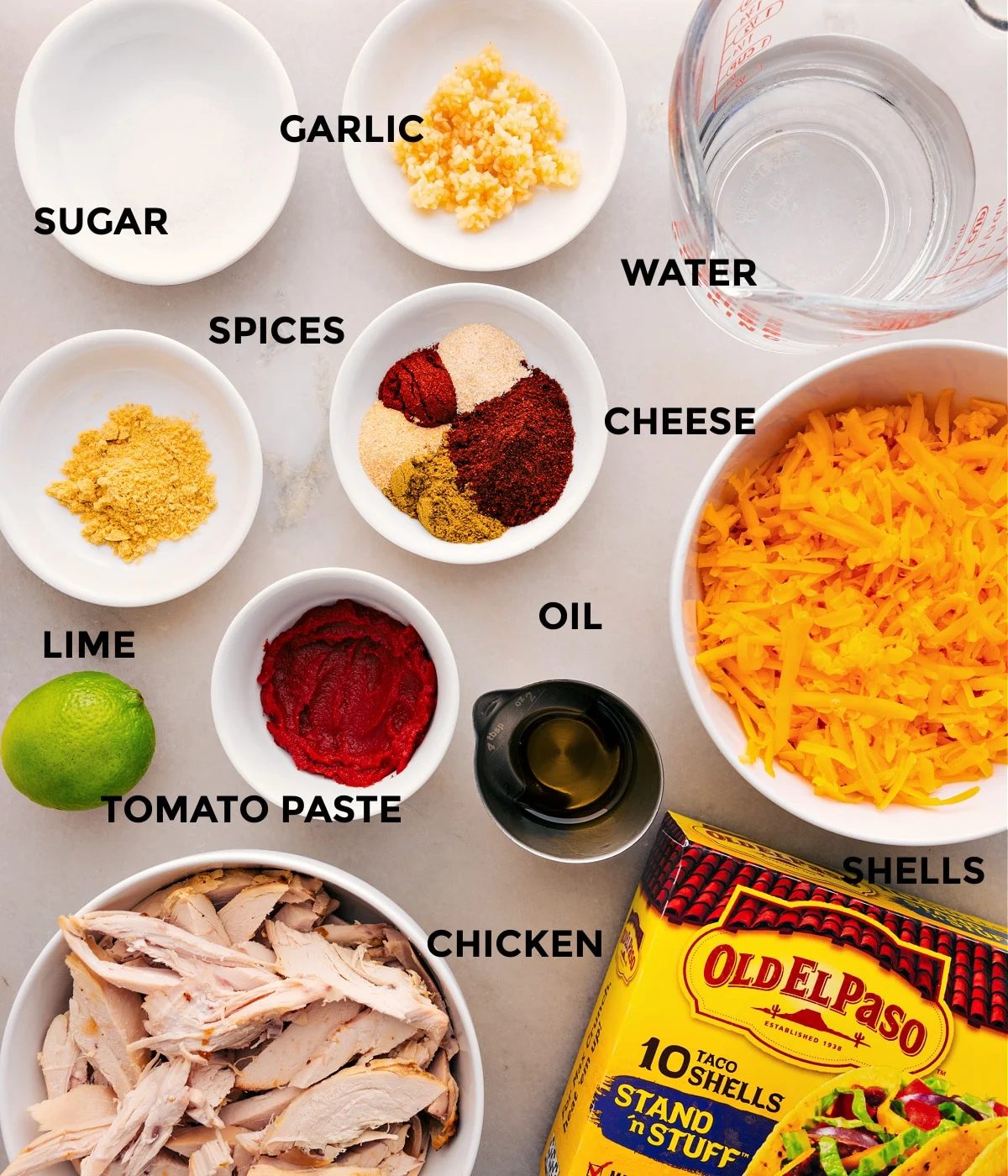 This recipe's ingredients are prepped for straightforward assembly: meat, water, cheese, shells, seasonings, tomato paste, lime, garlic, and sugar.