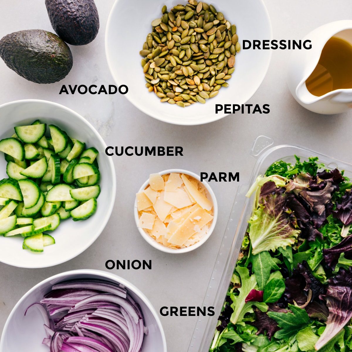 All the ingredients for this recipe—dressing, pepitas, avocado, cucumber, parm, greens, and onion—prepped and ready for straightforward assembly.