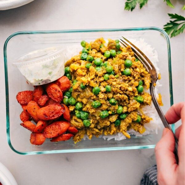 A meal-prepped tupperware container filled with rice, savory Indian ground turkey, roasted vegetables, and sauce, ready for a quick and satisfying meal.