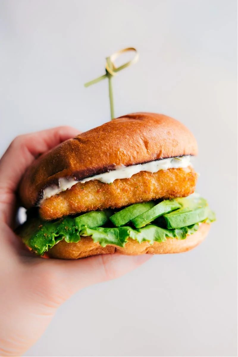 Fish sandwich with flaky fish, avocado, and lemon sauce on a toasted brioche bun.