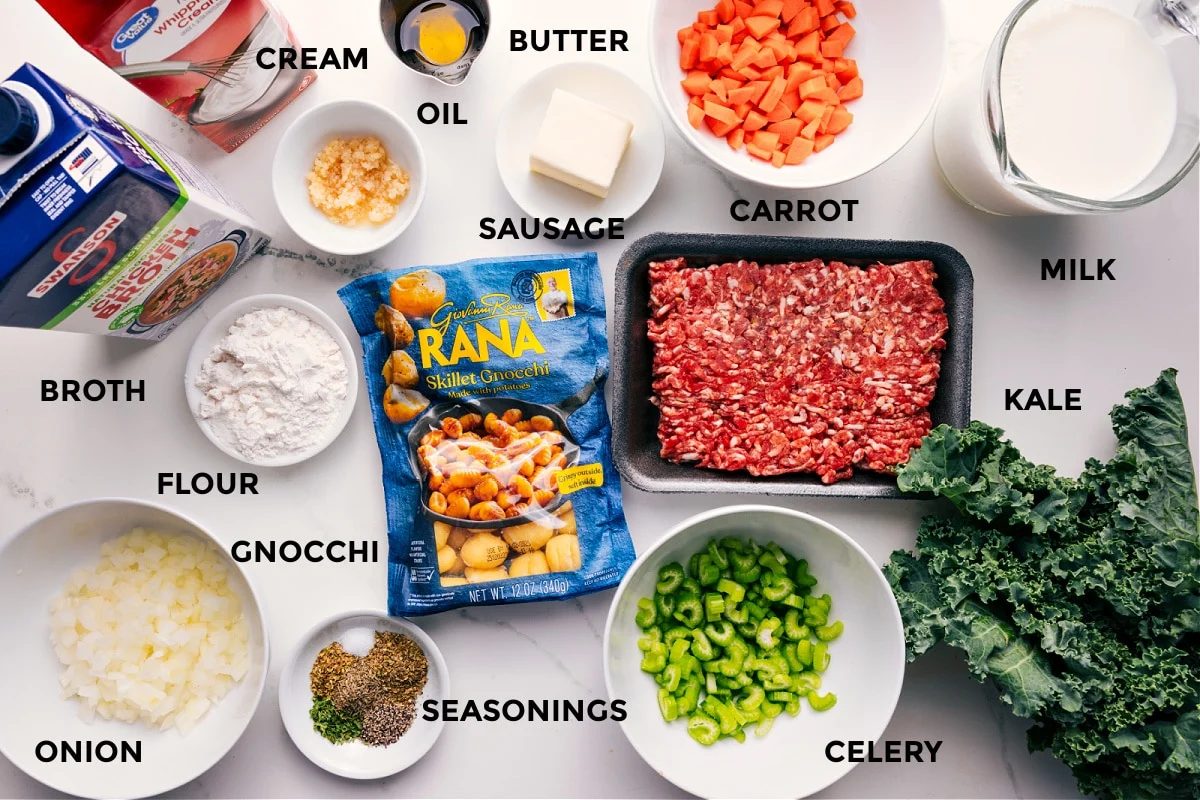 All the ingredients in this recipe prepped out for straightforward assembly including the broth, cream, flour, onion, gnocchi, seasonings, celery, kale, milk, carrot, sausage, butter, and oil.