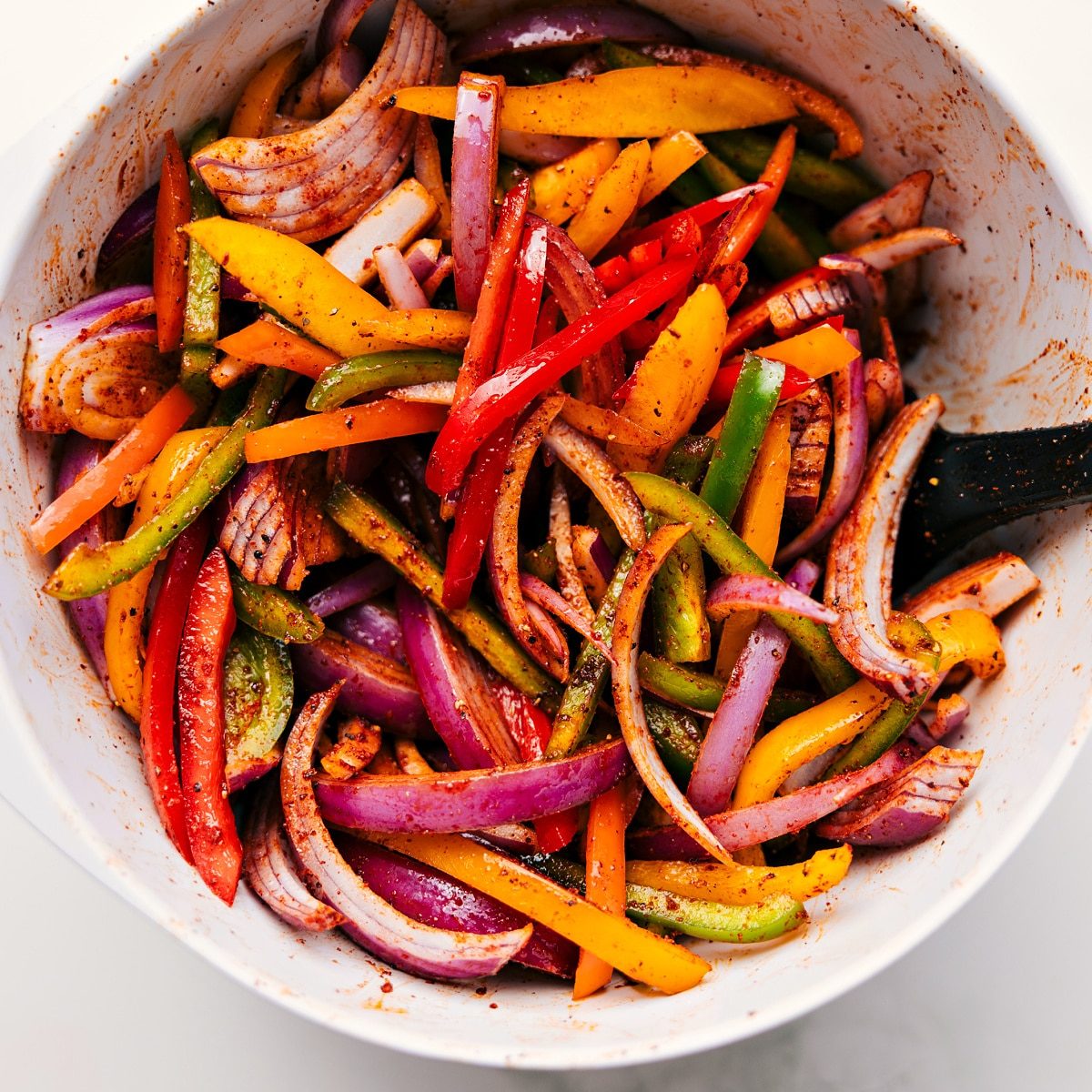 All the veggies chopped and tossed with the seasoning mix in a bowl for these sheet pan chicken fajitas.