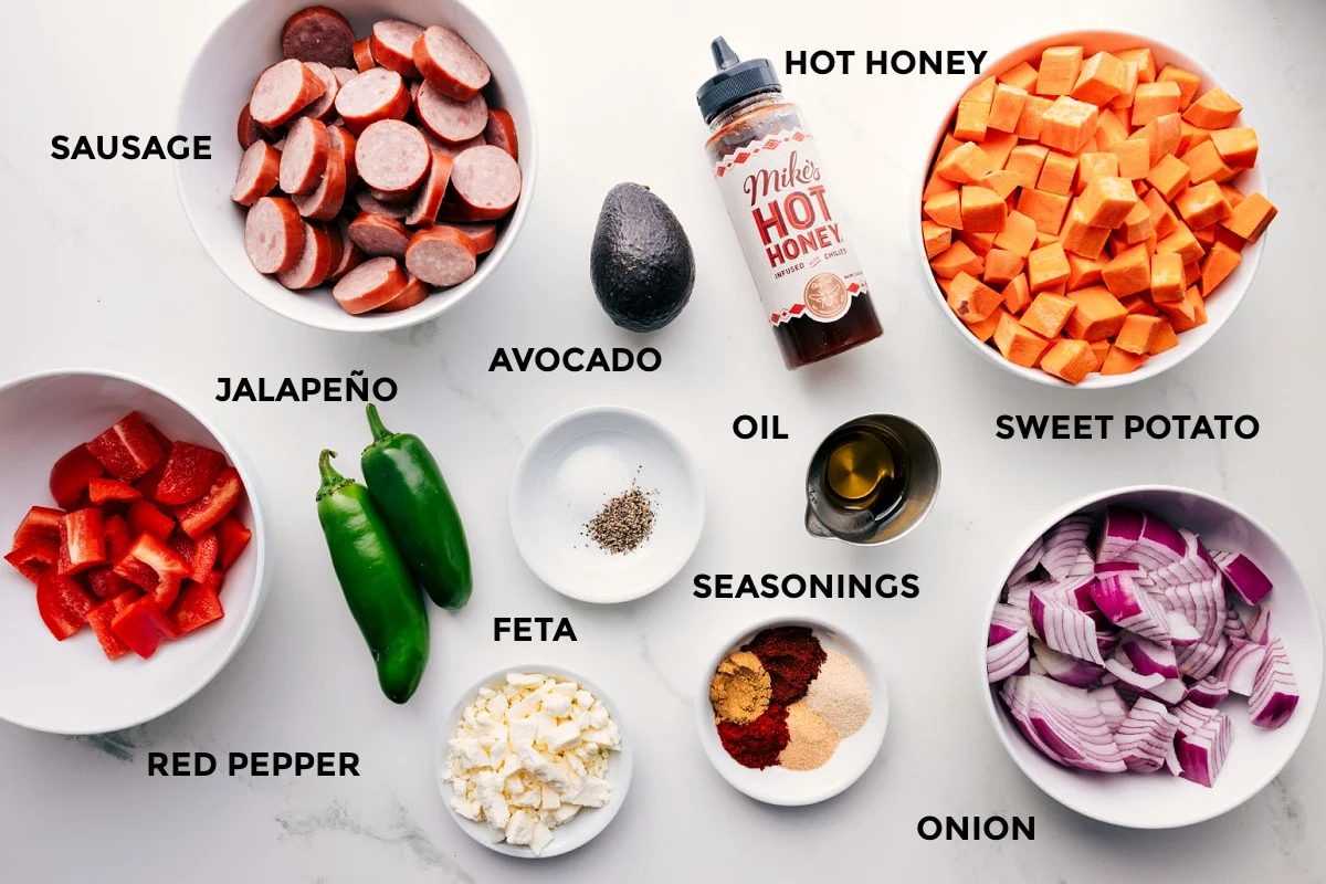 All the ingredients in this recipe prepped out for straightforward assembly including the red pepper, sausage, jalapeño, feta, avocado, seasonings, oil, hot honey, onion, and sweet potatoes.