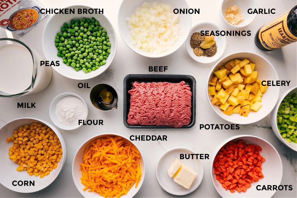 All the ingredients in this recipe prepped out for straightforward assembly including the chicken broth, peas, milk, corn, flour, oil, onion, seasonings, garlic, veggies, beef, and butter.