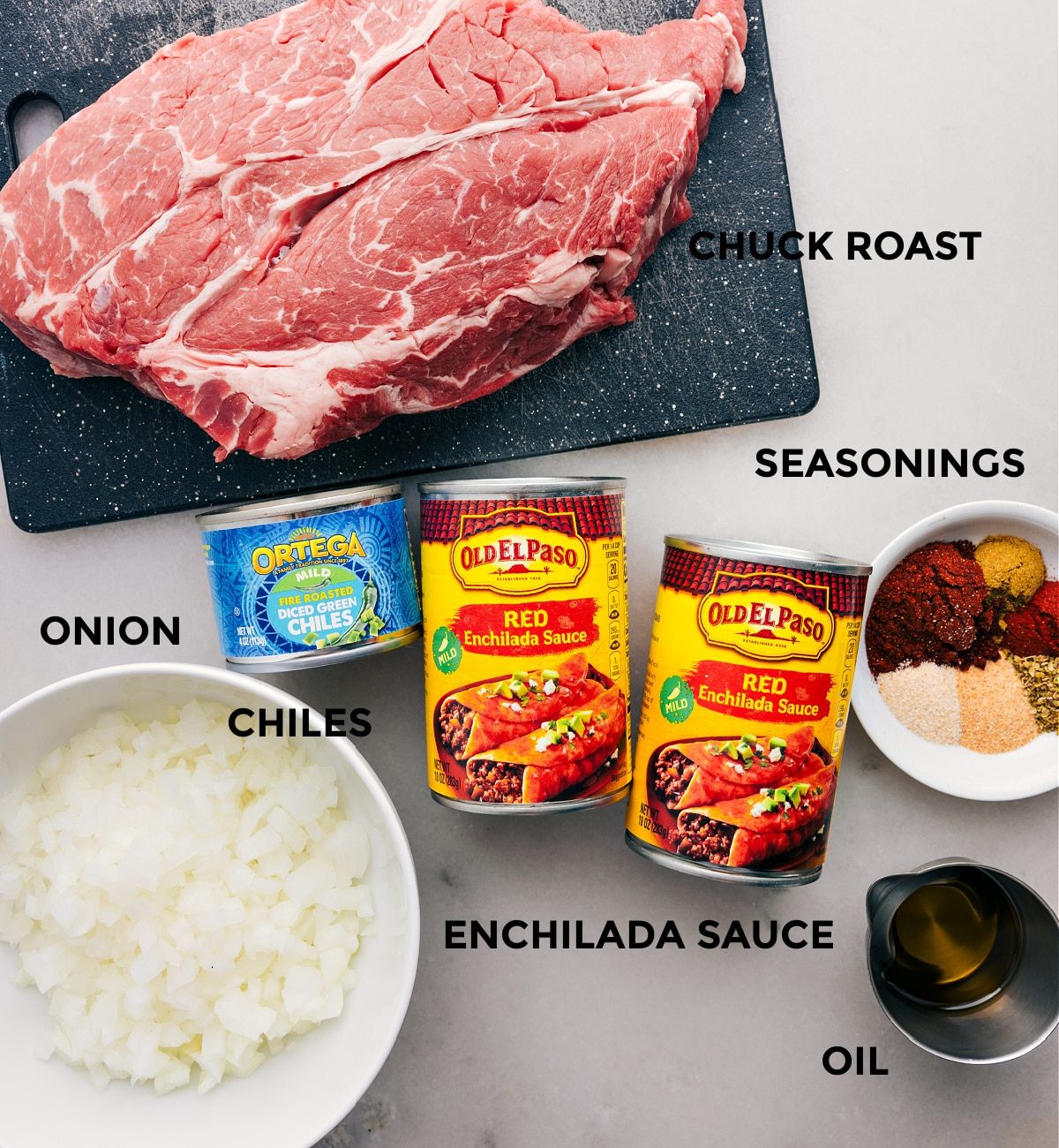 All the ingredients in this recipe prepped out for straightforward assembly including the meat, enchilada sauce, seasonings, onion, chiles, and oil.