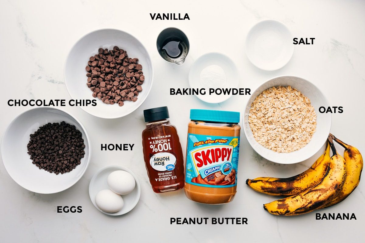 All the ingredients in this recipe prepped out for straightforward assembly including the chocolate chips, eggs, honey, peanut butter, bananas, oats, baking powder, salt, and vanilla.