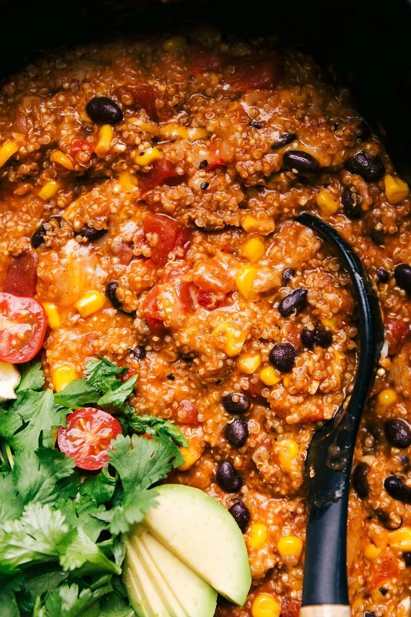 Finished enchilada quinoa dish in a slow cooker, rich and flavorful, with a spoon nestled inside, ready for serving.