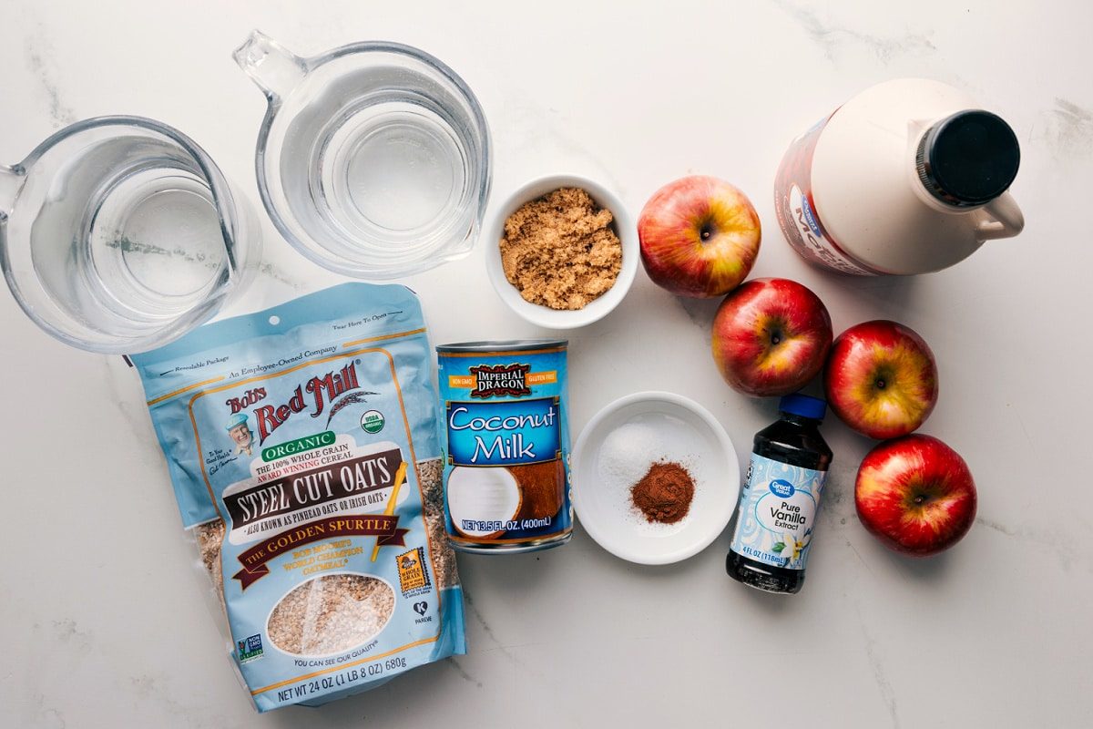 All the ingredients in this recipe prepped out for straightforward assembly including the apples, oats, coconut milk, water, brown sugar, maple syrup, cinnamon, salt, and vanilla.