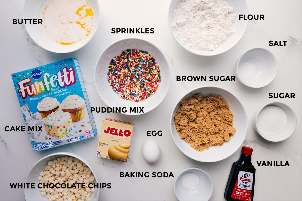 All the ingredients for this recipe prepped and ready for straightforward assembly, including butter, cake mix, sprinkles, pudding mix, flour, salt, sugar, brown sugar, vanilla, baking soda, and white chocolate chips.
