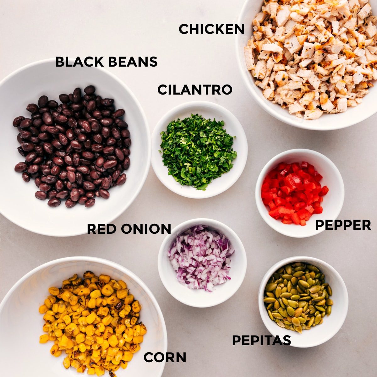 All the ingredients in this recipe are prepped for straightforward assembly: meat, peppers, cilantro, black beans, red onion, pepitas, and corn.