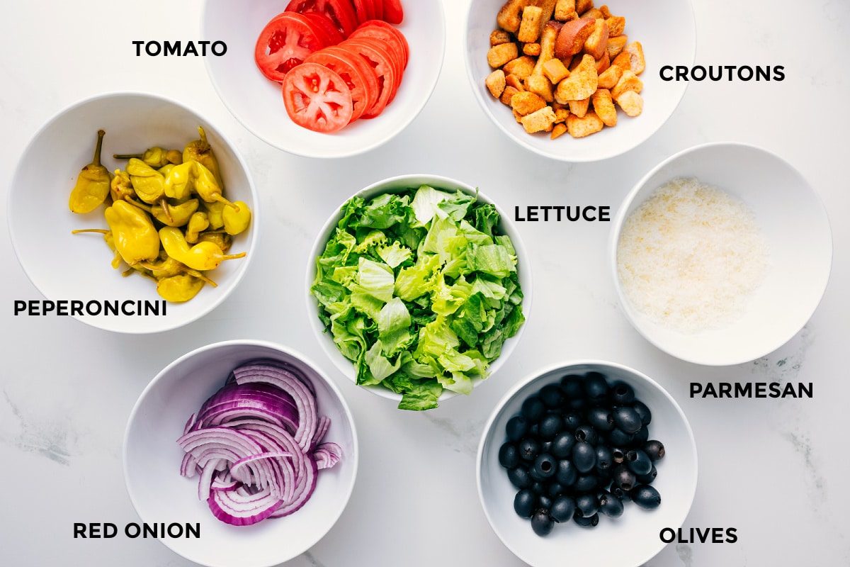 All the ingredients in this recipe prepped out for straightforward assembly including the peperoncini, red onion, tomato, lettuce, olives, parmesan, and croutons.