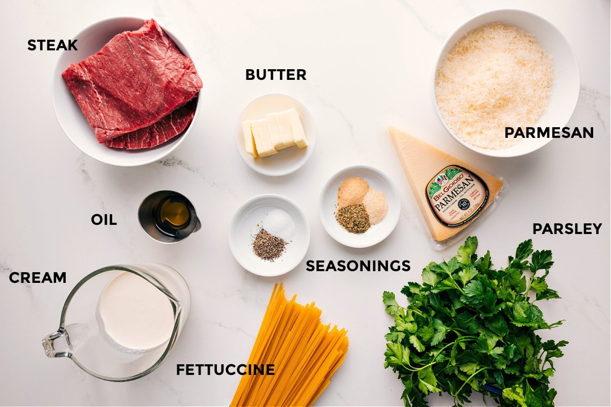 All the ingredients in this recipe prepped out for straightforward assembly including the steak, butter, oil, cream, seasonings, fettuccine, parsley, and parmesan.