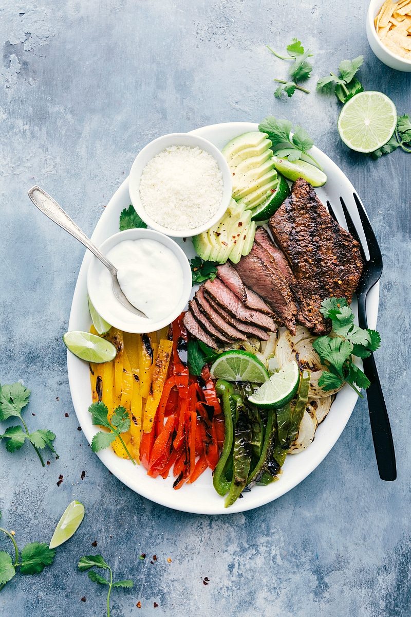 Steak Fajita Recipe with all the mixings like fresh avocado, lime, cilantro, sour cream, and cheese.