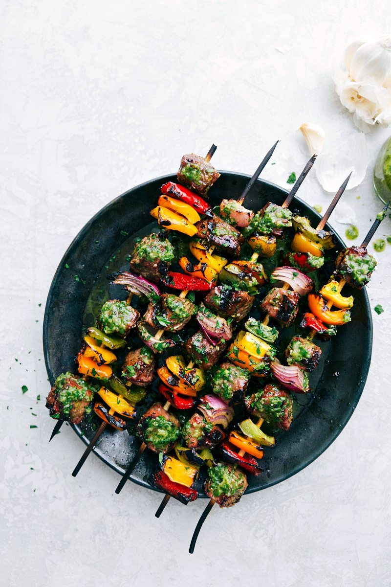 Plate of steak kebabs with basil sauce on top.