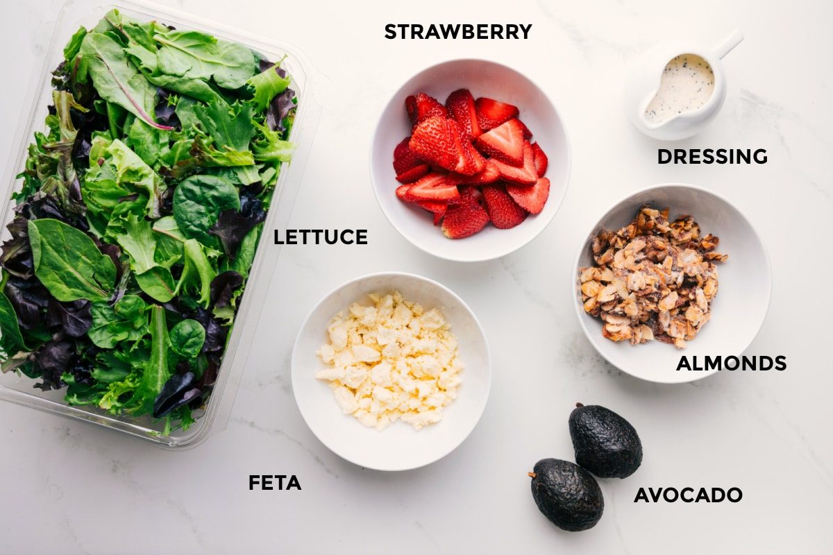 Ingredients for this recipe prepped and ready for straightforward assembly, including the fruit, dressing, almonds, avocado, feta, and lettuce.