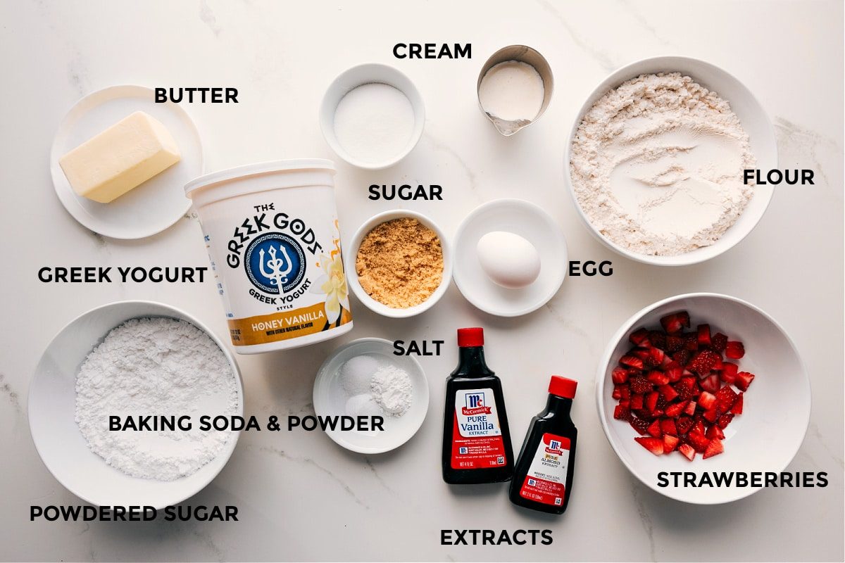 All the ingredients in this recipe prepped out for straightforward assembly including the butter, yogurt, powdered sugar, baking agents, sugar, cream, egg, flour, extracts, and strawberries.