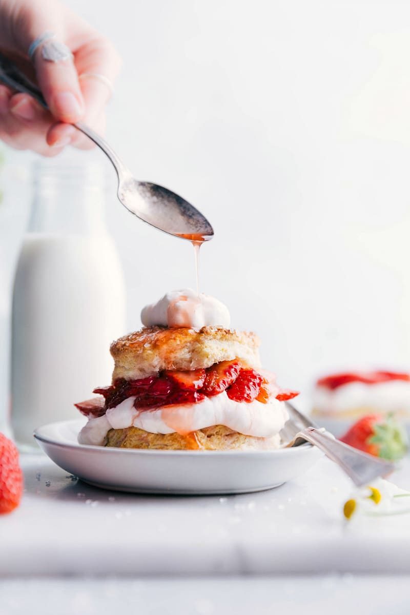 Moist and satisfying strawberry shortcake with layers of fluffy cake, fresh strawberries, and whipped cream, strawberry sauce being drizzled on top.