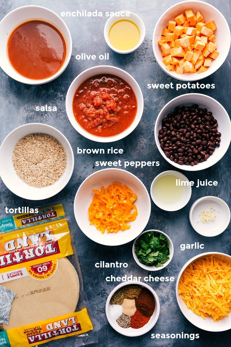 All the ingredients in this recipe prepped out for straightforward assembly including the enchilada sauce, oil, sweet potatoes, salsa, black beans, peppers, rice, lime, garlic, cilantro, cheese, seasonings, and tortillas.