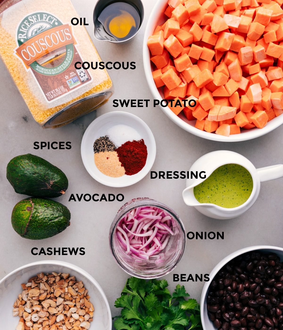 All the ingredients for this recipe are prepped and ready for straightforward assembly, including sweet potatoes, couscous, dressing, onion, avocado, cashews, and black beans.