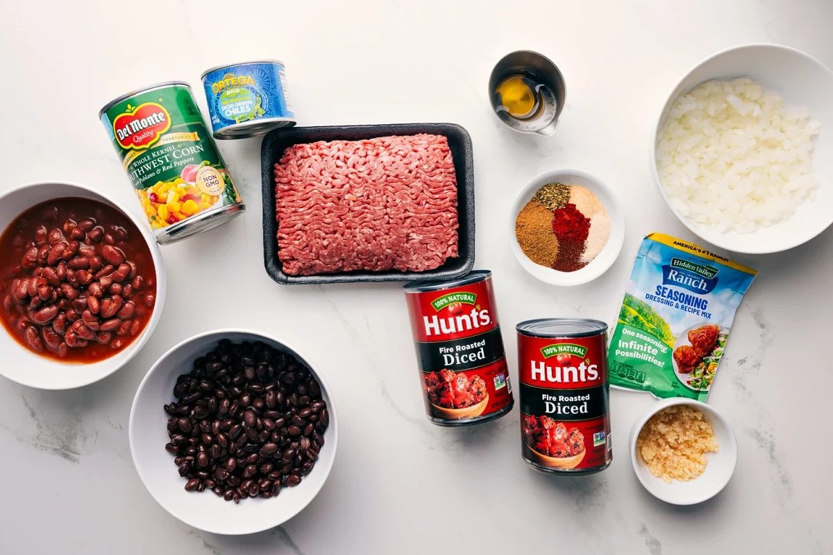 All the ingredients in this recipe prepped out for straightforward assembly including the beans, corn, chiles, beef, tomatoes, seasonings, oil, garlic, and onions.
