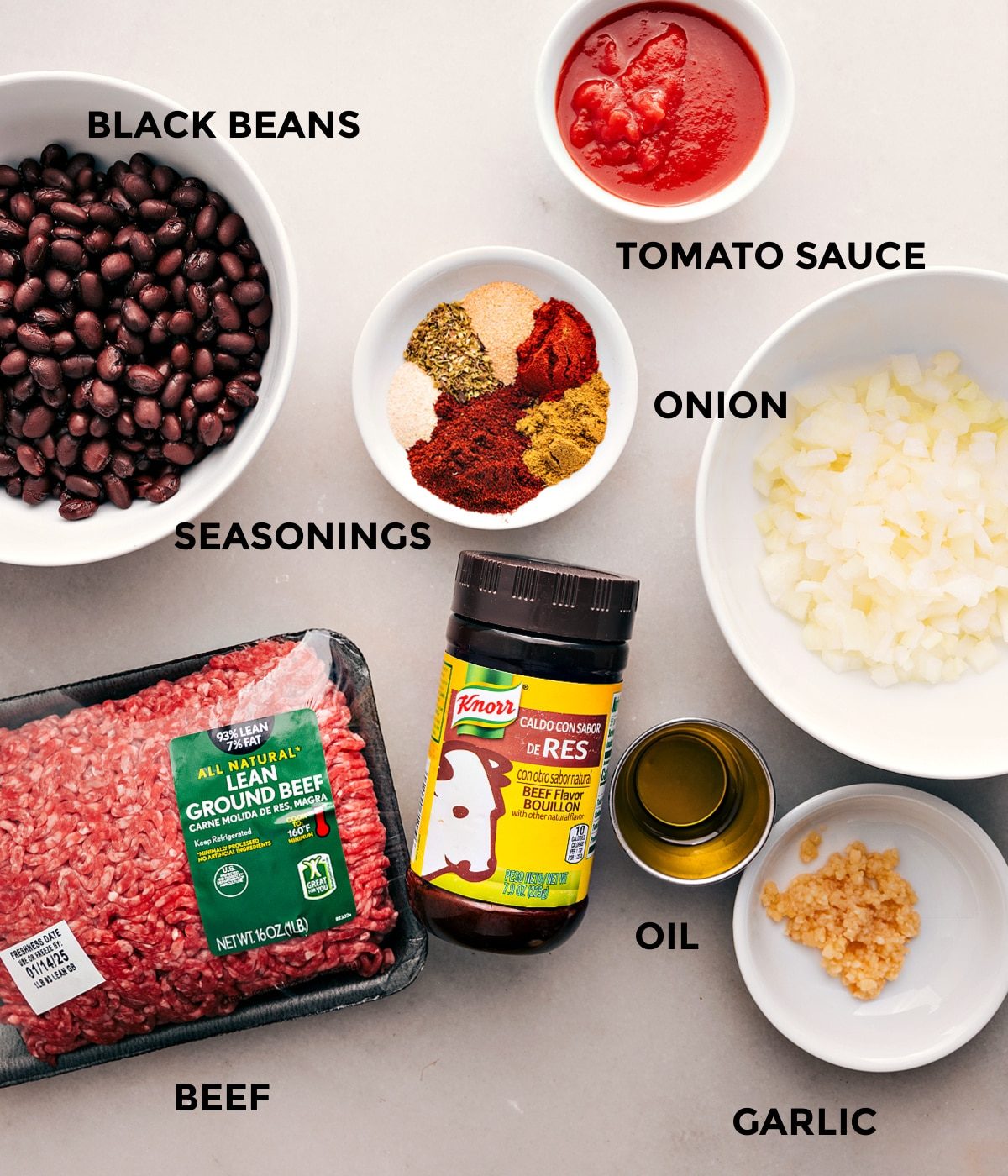 All the ingredients for this recipe are prepped and ready for straightforward assembly, including tomato sauce, beef, onion, black beans, seasonings, oil, and garlic.