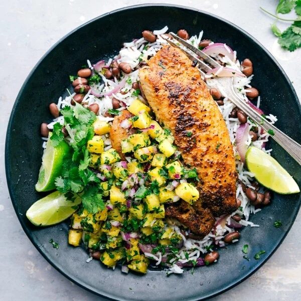 A plate featuring blackened tilapia served with pineapple salsa, rice, and black beans, presenting a flavor-packed and satisfying meal.