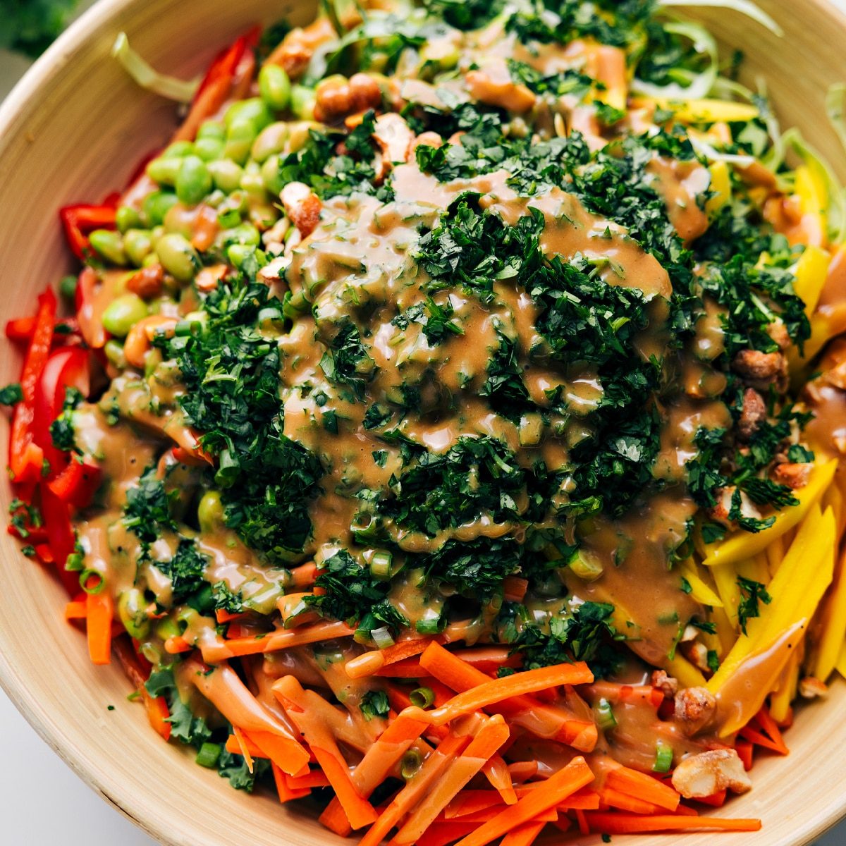 Thai Quinoa Salad in a large bowl with the ingredients layered and dressing drizzled over the top before tossing.